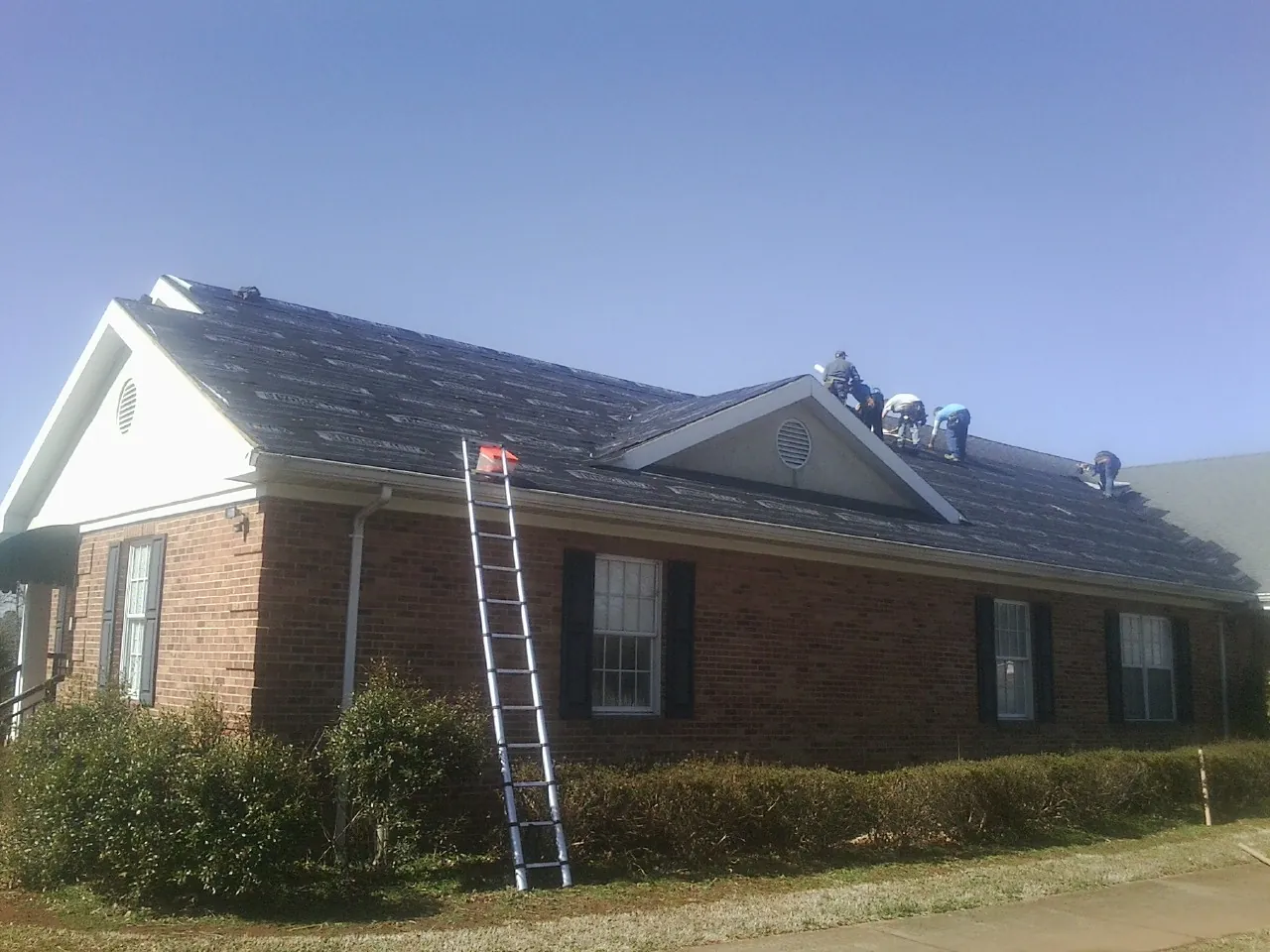 Crew tearing shingles off a brick ranch roof with a ladder set — Emergency Roof Repair work by our crew in Whipple