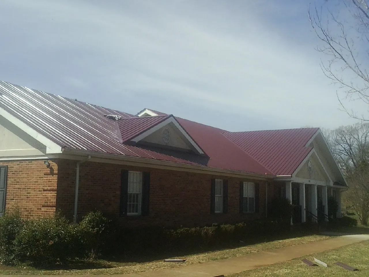 Red metal roof with gabled entries on a long brick building, from a Hail Damage Roof Repair job in Whipple