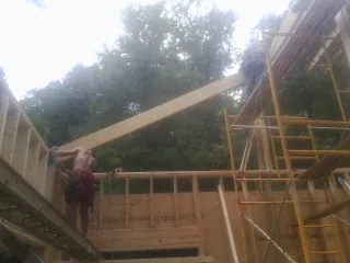 Carpenter raising a rafter beam on a new second story frame in Whipple