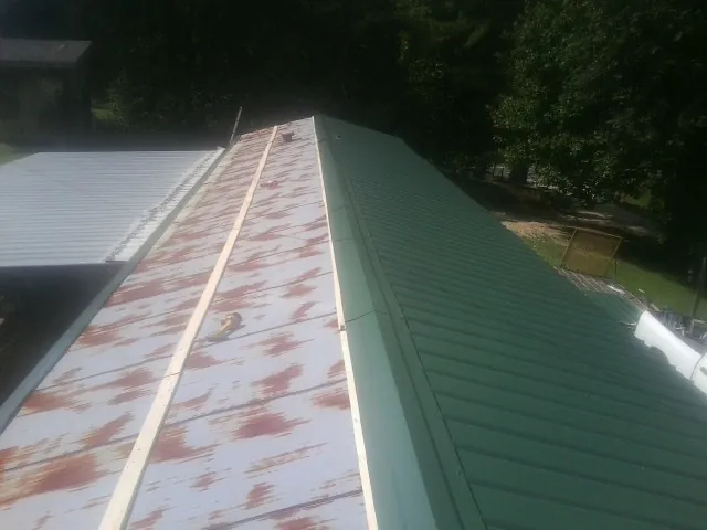 Old rusted panels beside newly installed green metal roofing — Wind Damage Roof Repair by Roofing Brothers in Whipple