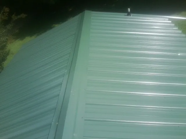 New green metal panels meeting at the ridge of a roof — Flat Roof Repair work by our crew in Whipple