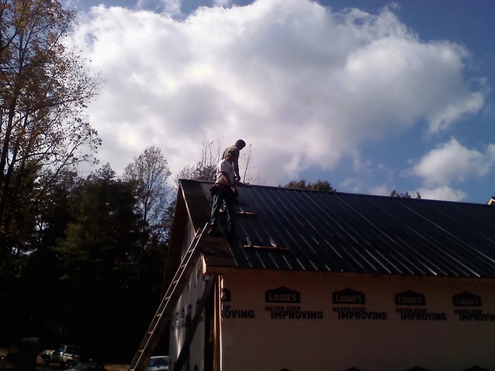 Roofer fastening dark metal panels high against a cloudy sky, from a Roof Inspection job in Whipple
