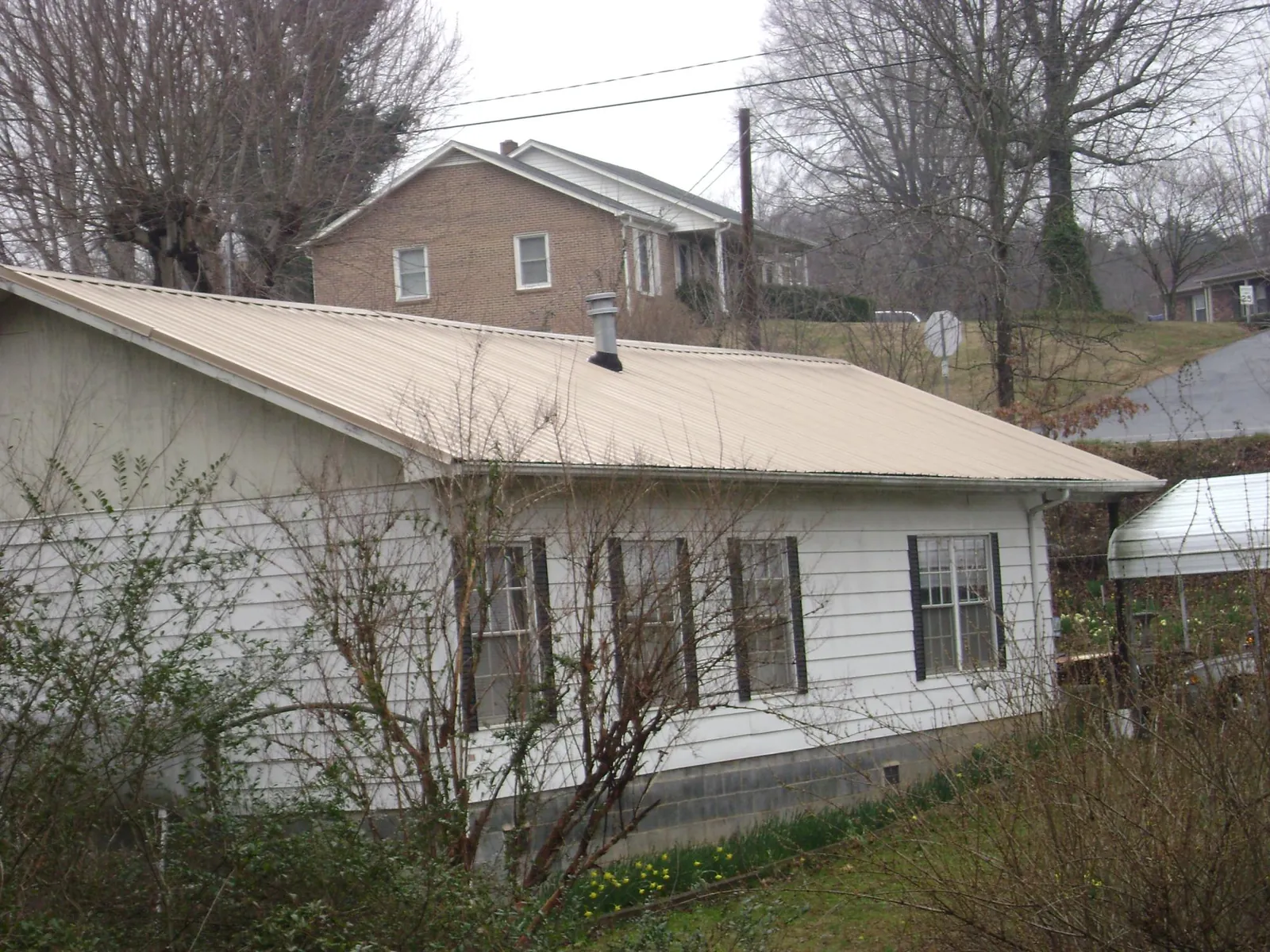Tan metal roof on a white sided house set into a hillside — Commercial Roofing by Roofing Brothers in Whipple