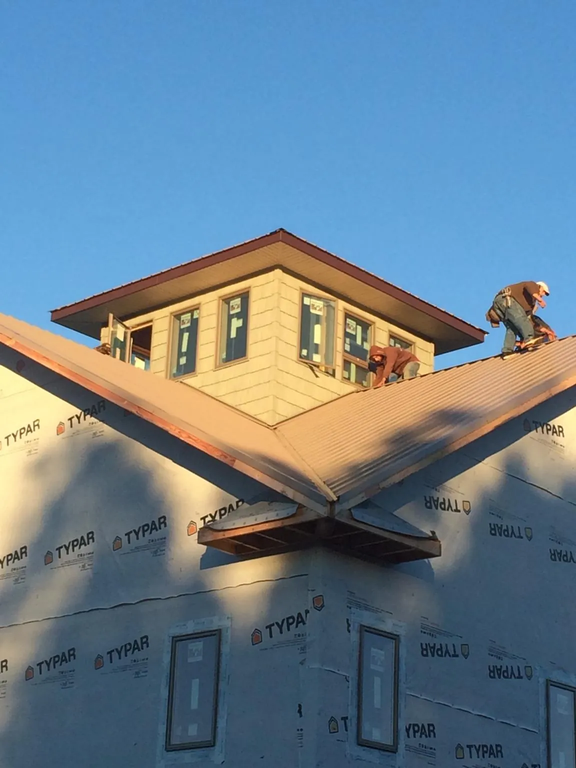 Roofers working around a rooftop cupola on a new metal roof at sunset — Roof Waterproofing in Whipple by Roofing Brothers